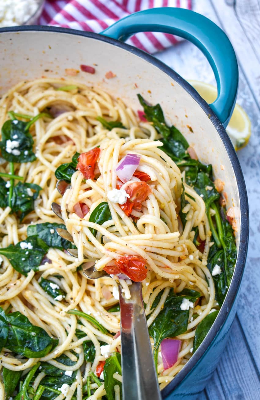 a slotted silver spoon holding a scoop of easy greek spaghetti above a dutch oven