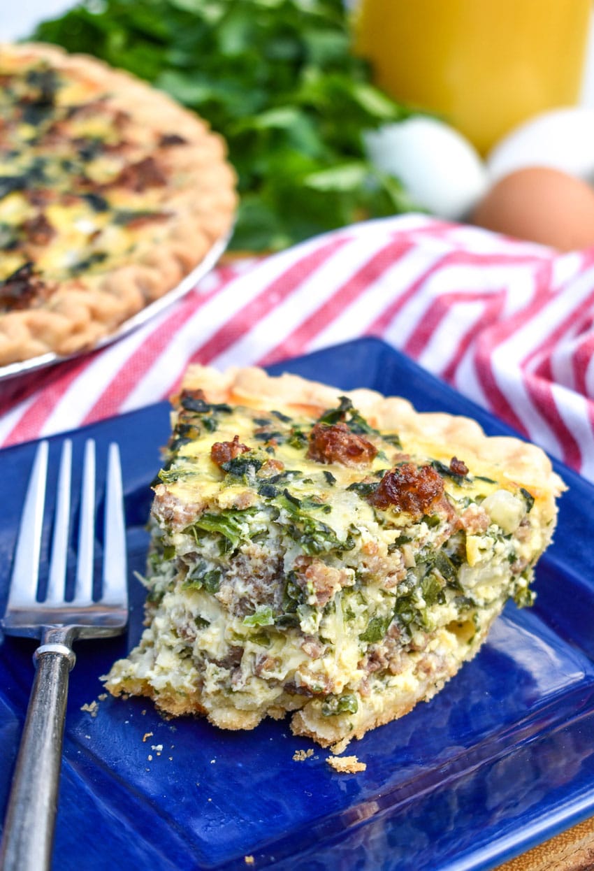 a slice of spinach and sausage quiche on a small bule square plate with a silver fork on the side