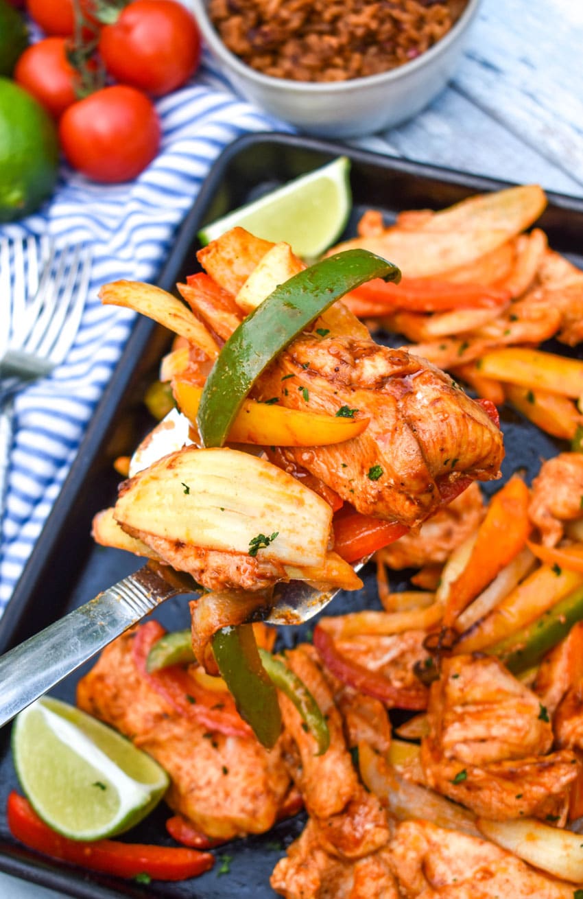 a silver spatula scooping chicken and vegetable fajita mixture off of a metal sheet pan