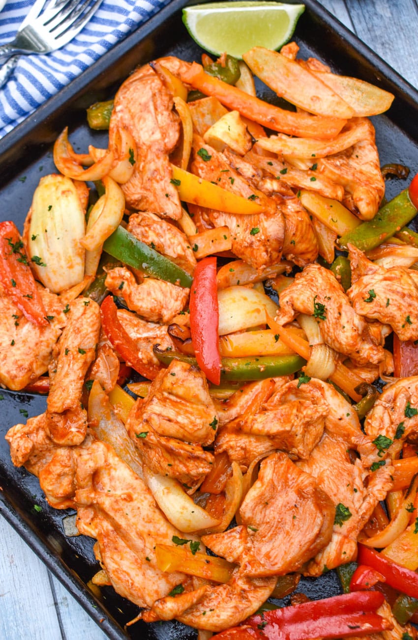 sheet pan chicken fajitas on a metal baking sheet with fresh lime edges on the side