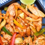 sheet pan chicken fajitas on a metal baking sheet with fresh lime edges on the side