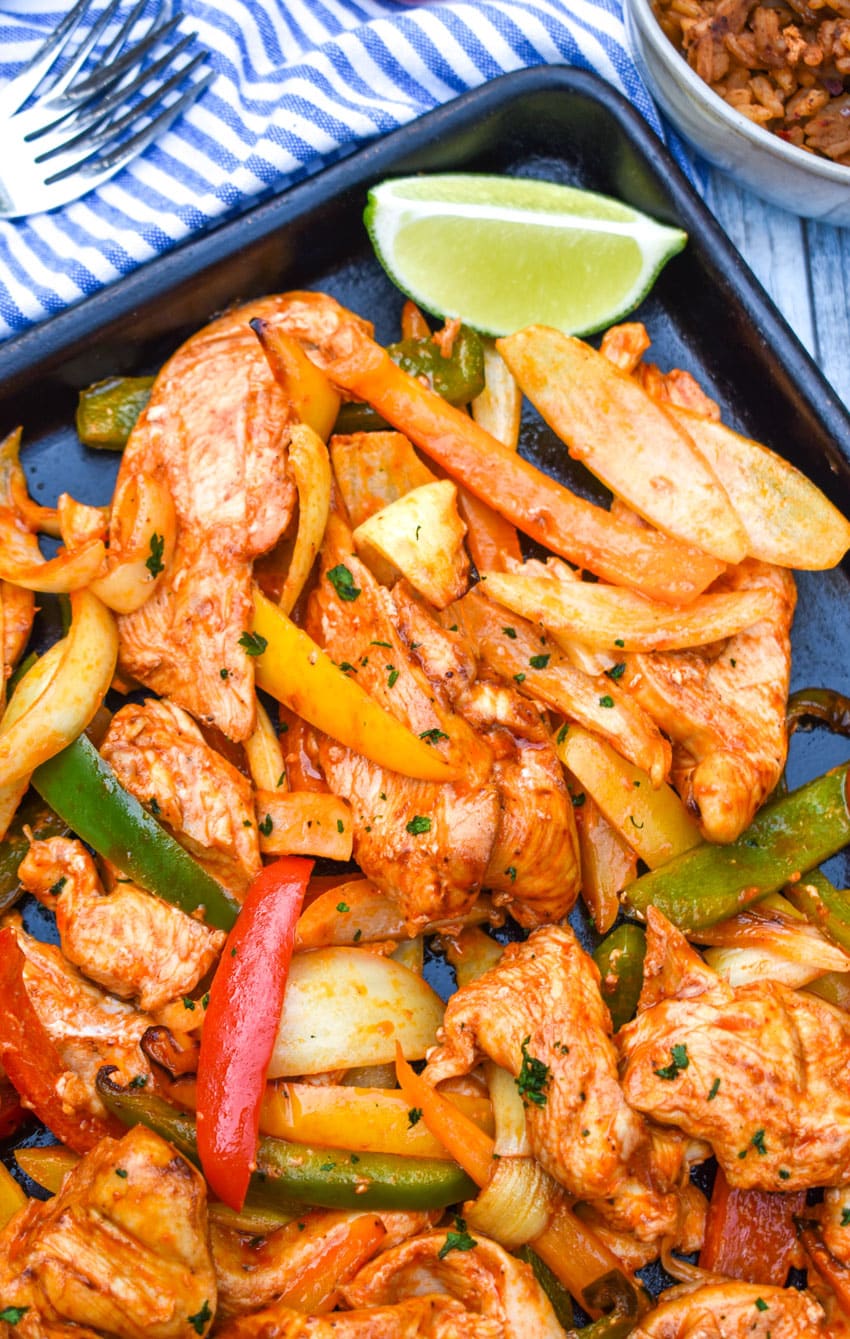 sheet pan chicken fajitas on a metal baking sheet with fresh lime edges on the side