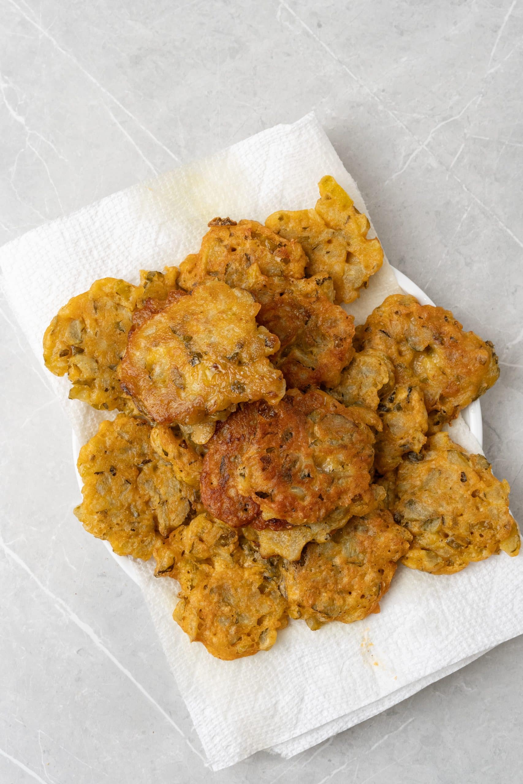 a pile of fried dill pickle fritters draining on a paper towel lined plate