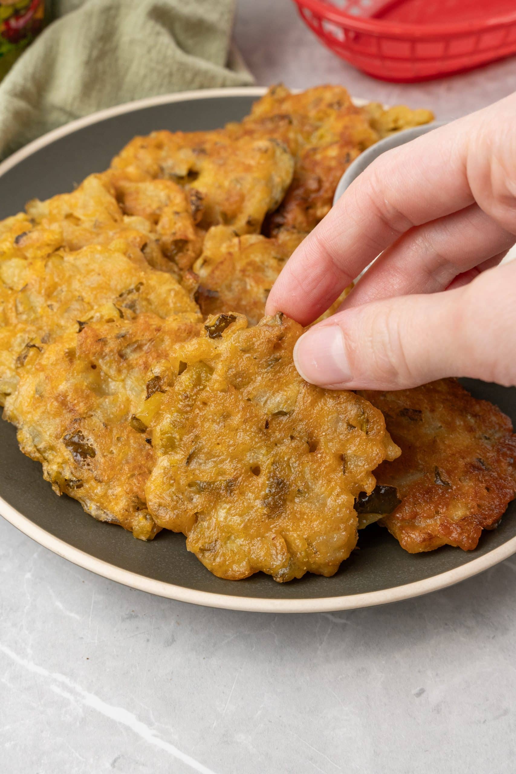 a hand picking up a fried dill pickle fritter off of a brown plate