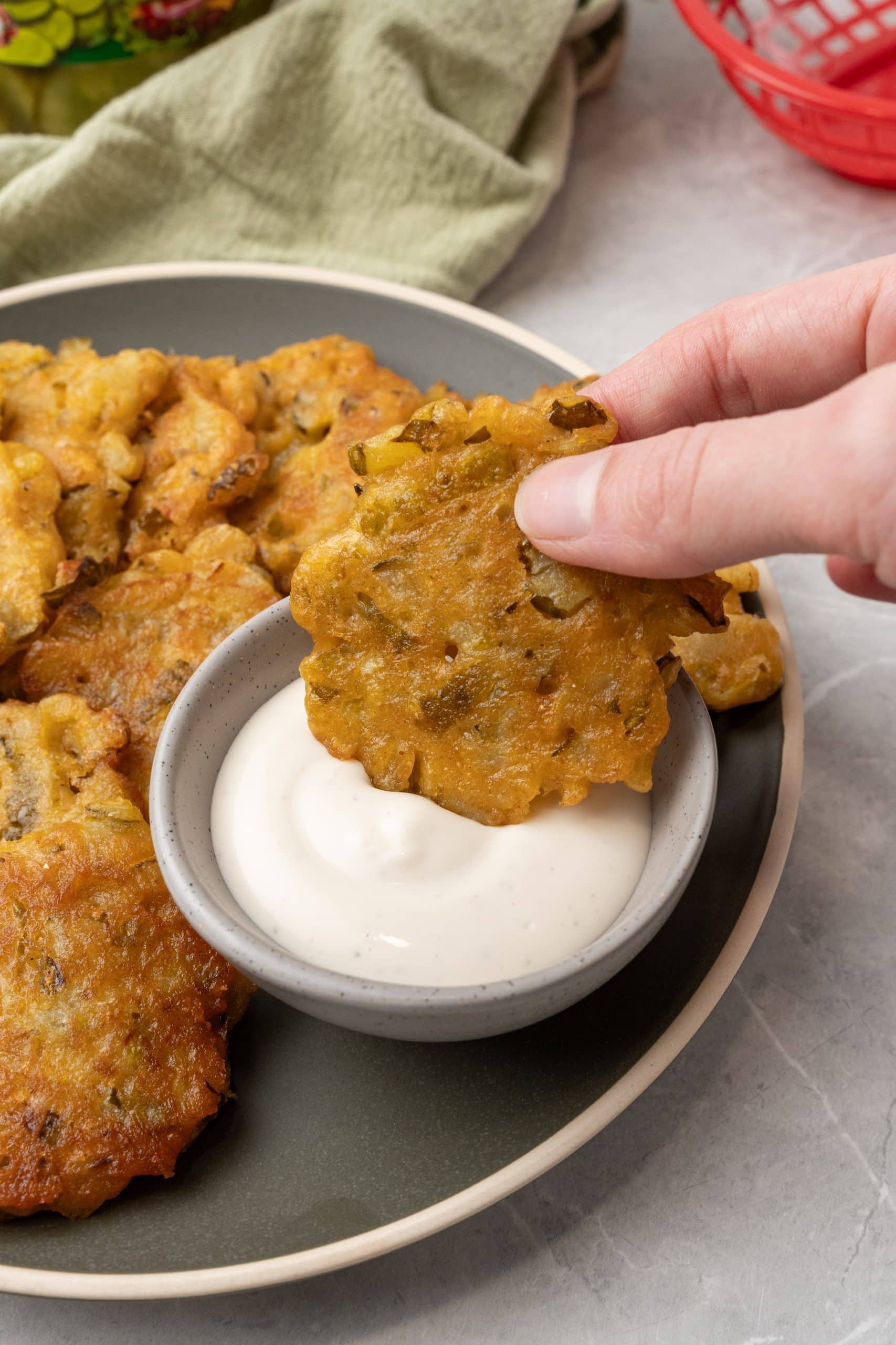 a hand holding a dill pickle fritter being dipped into a small gray bowl filled with ranch dressing