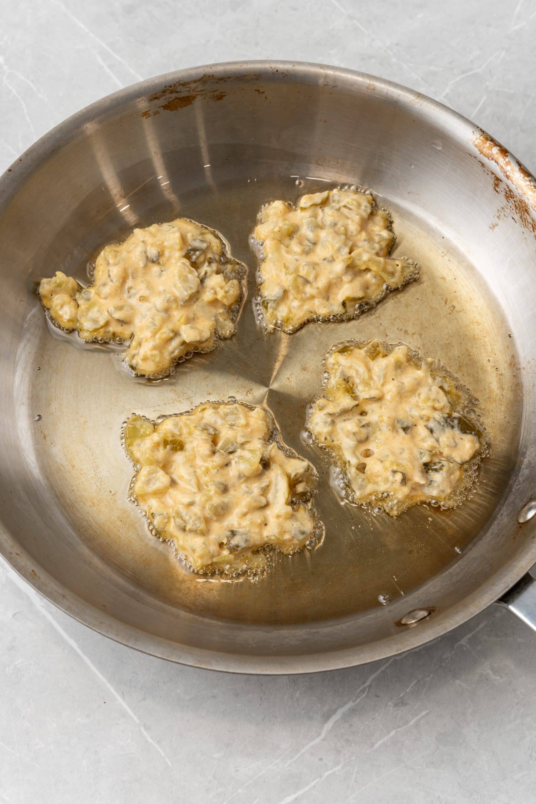 dill pickle fritters frying in a metal sauce pan in hot oil