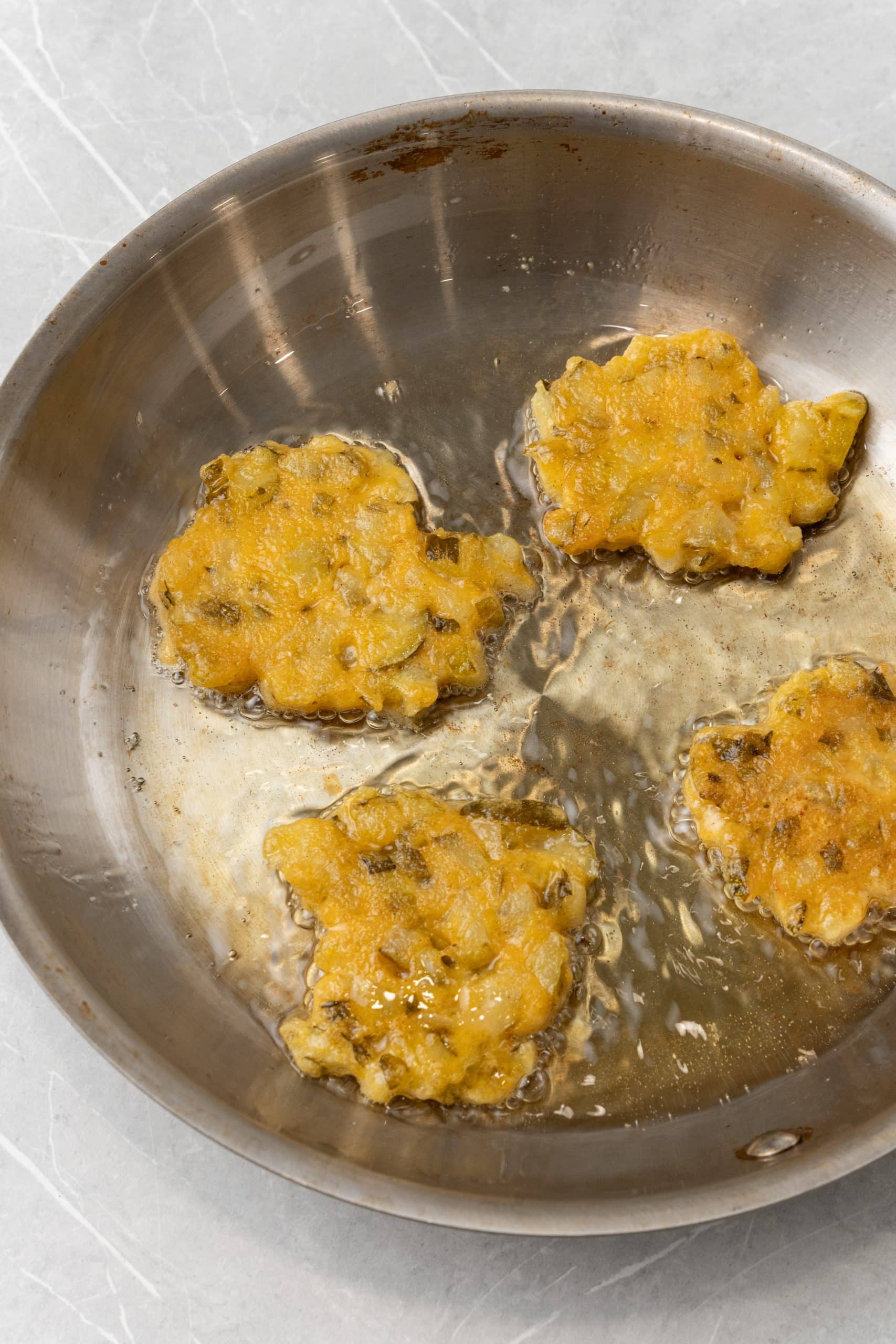 dill pickle fritters frying in a metal sauce pan in hot oil