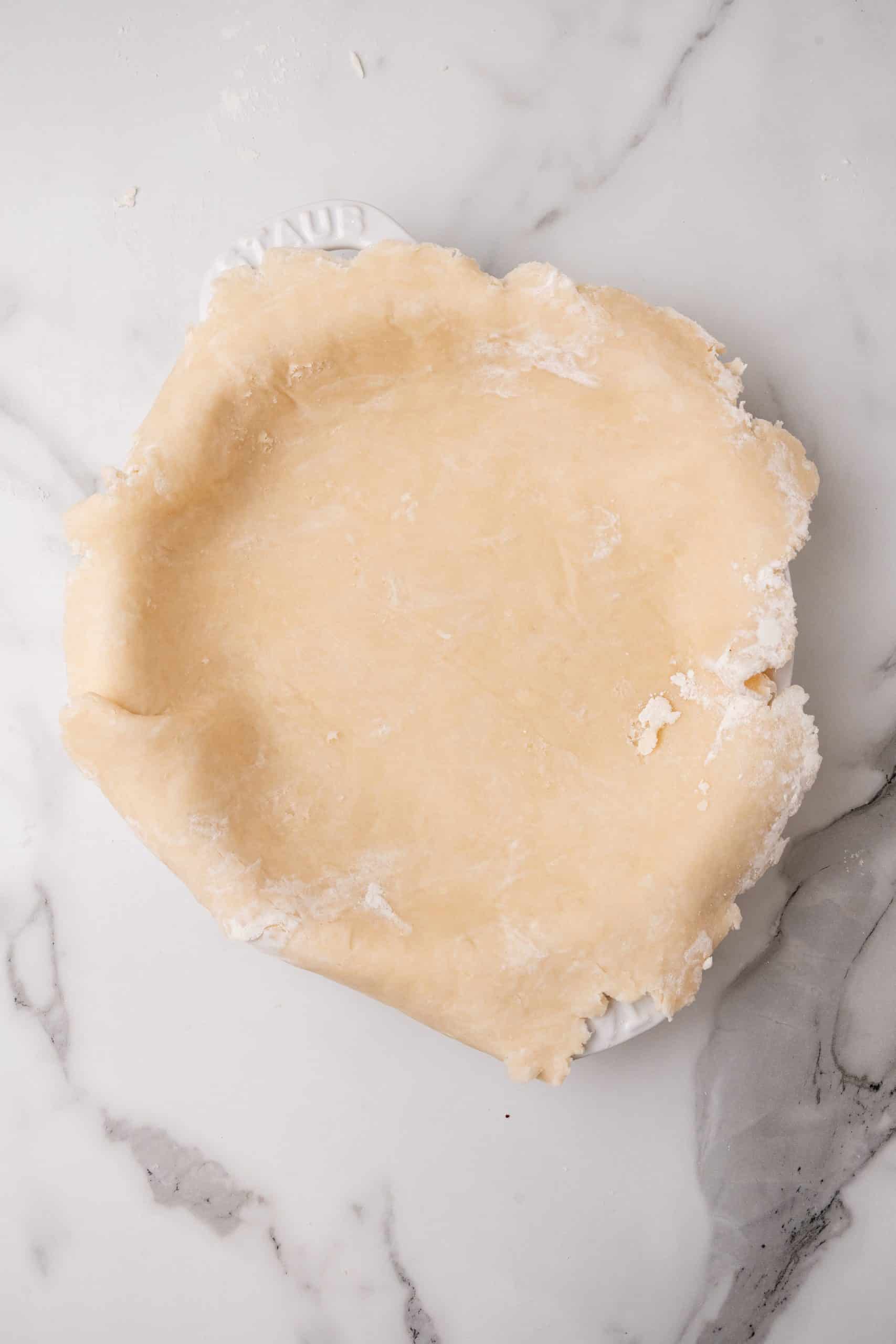 an easy homemade pie crust laid out over the edges of a white pie dish