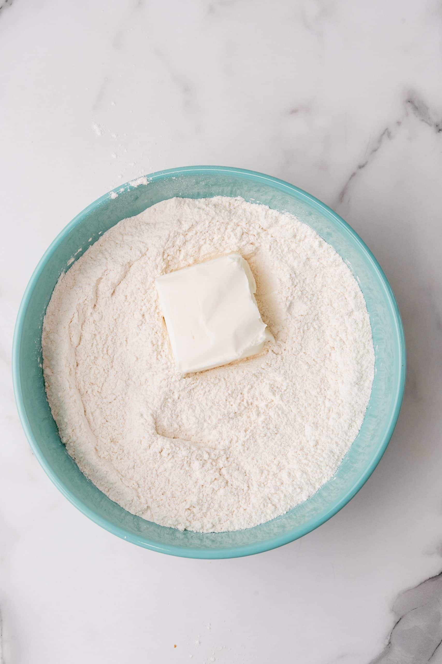 a square of lard resting on salted flour in the bottom of a blue mixing bowl