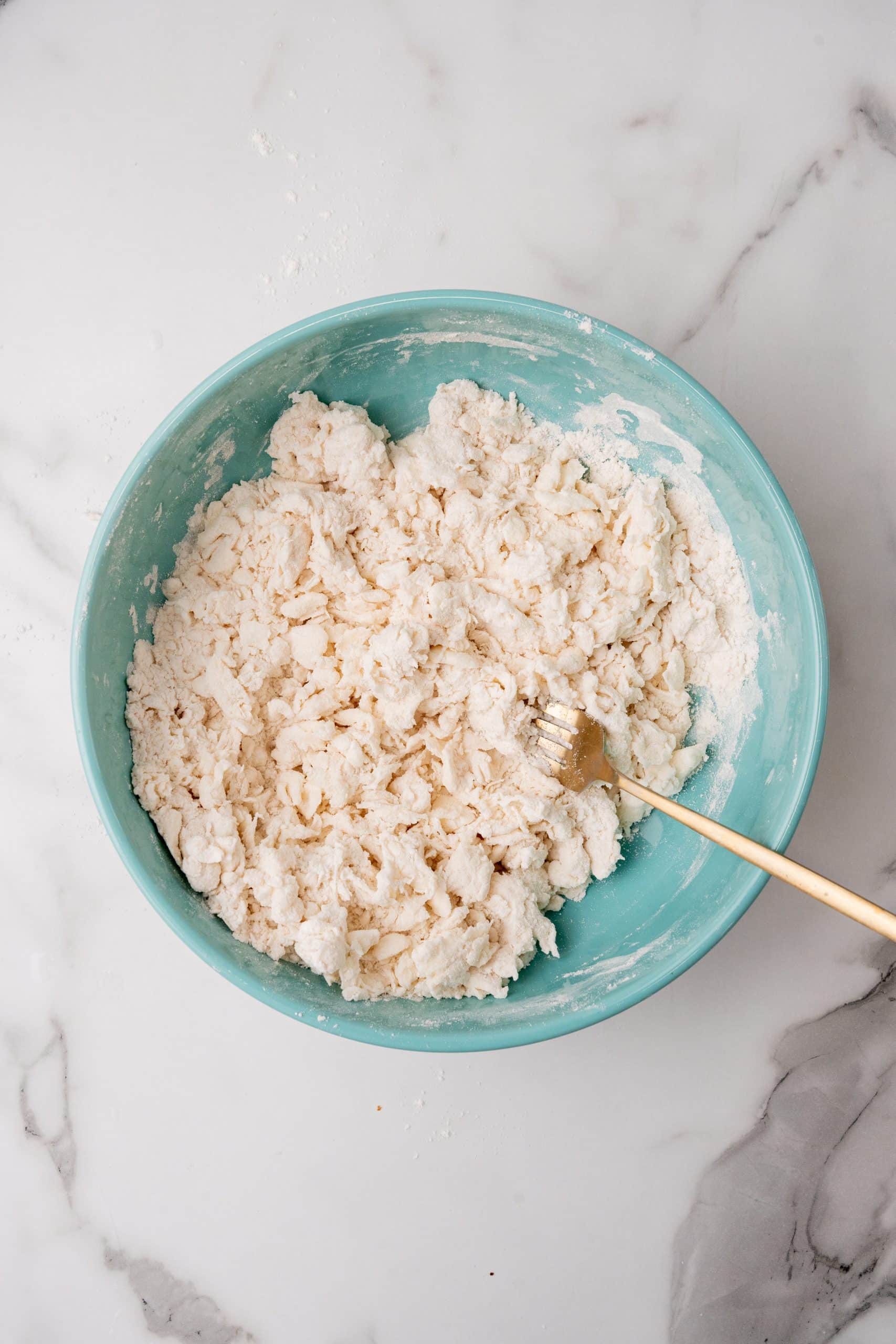 a gold fork resting on the edge of a blue bowl filled with pie dough