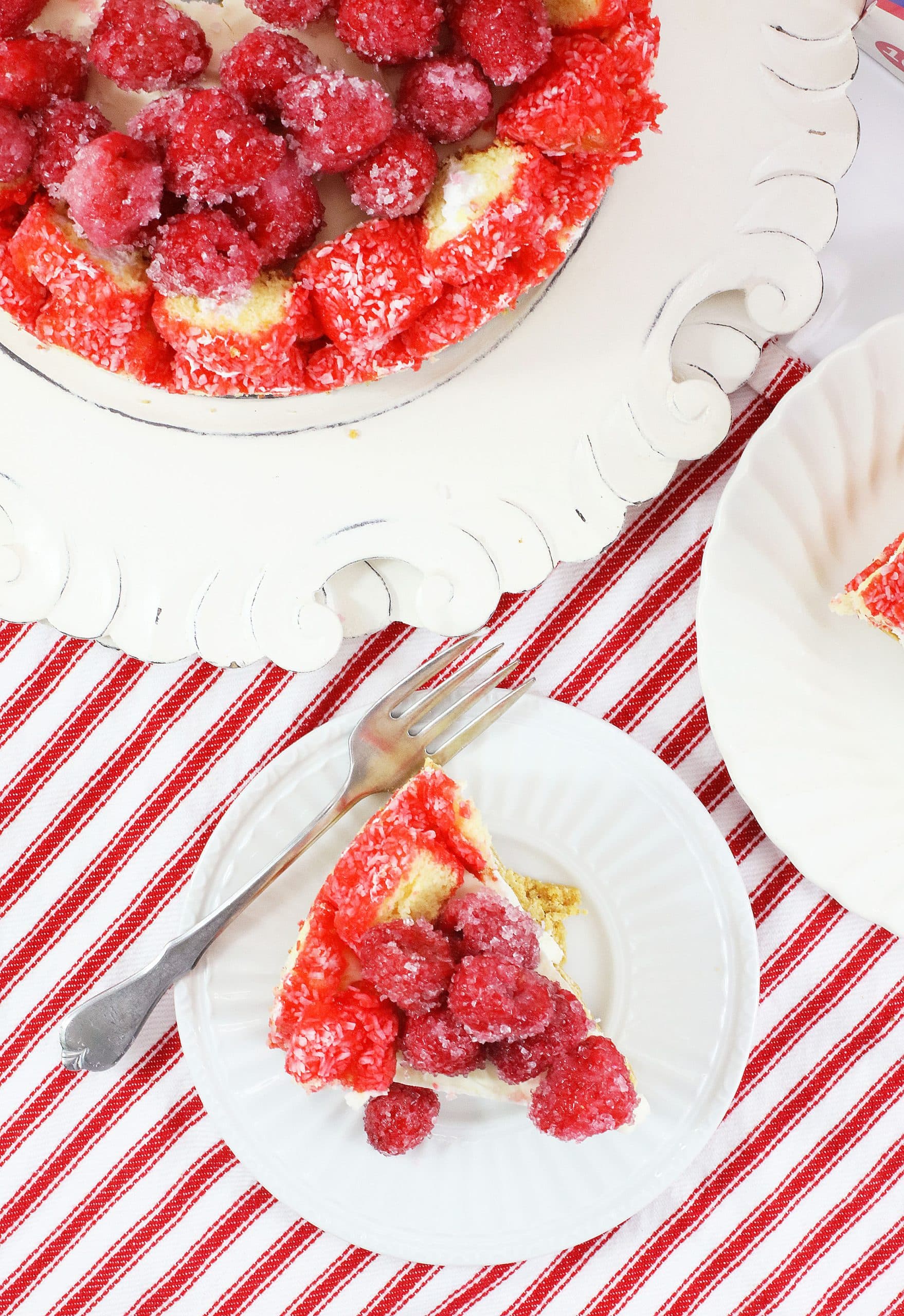 a slice of raspberry zinger cheesecake on a small white dessert plate with a silver fork on the side