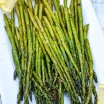 stalks of air fryer roasted asparagus on a white serving platter with slices of lemon on the side