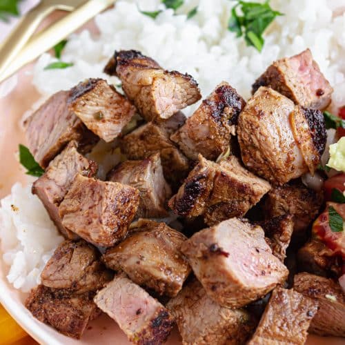 a close up of copycat chipotle steak strips next to steamed white rice in a white bowl