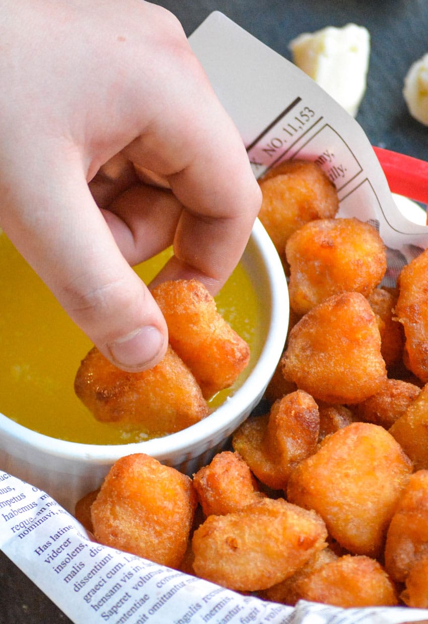 a hand dipping two fried cheese curds into a bowl of garlic butter