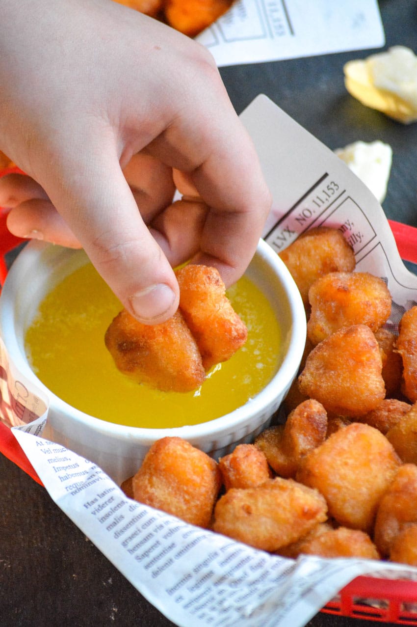 a hand dipping two fried cheese curds into a bowl of garlic butter