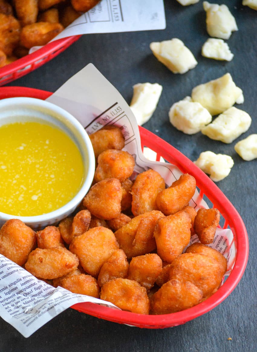 fried cheese curds in a paper lined plastic food basket with a bowl of garlic butter on the side