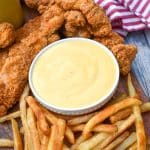 homemade honey mustard sauce in a small white dipping bowl surrounded by chicken tenders and french fries
