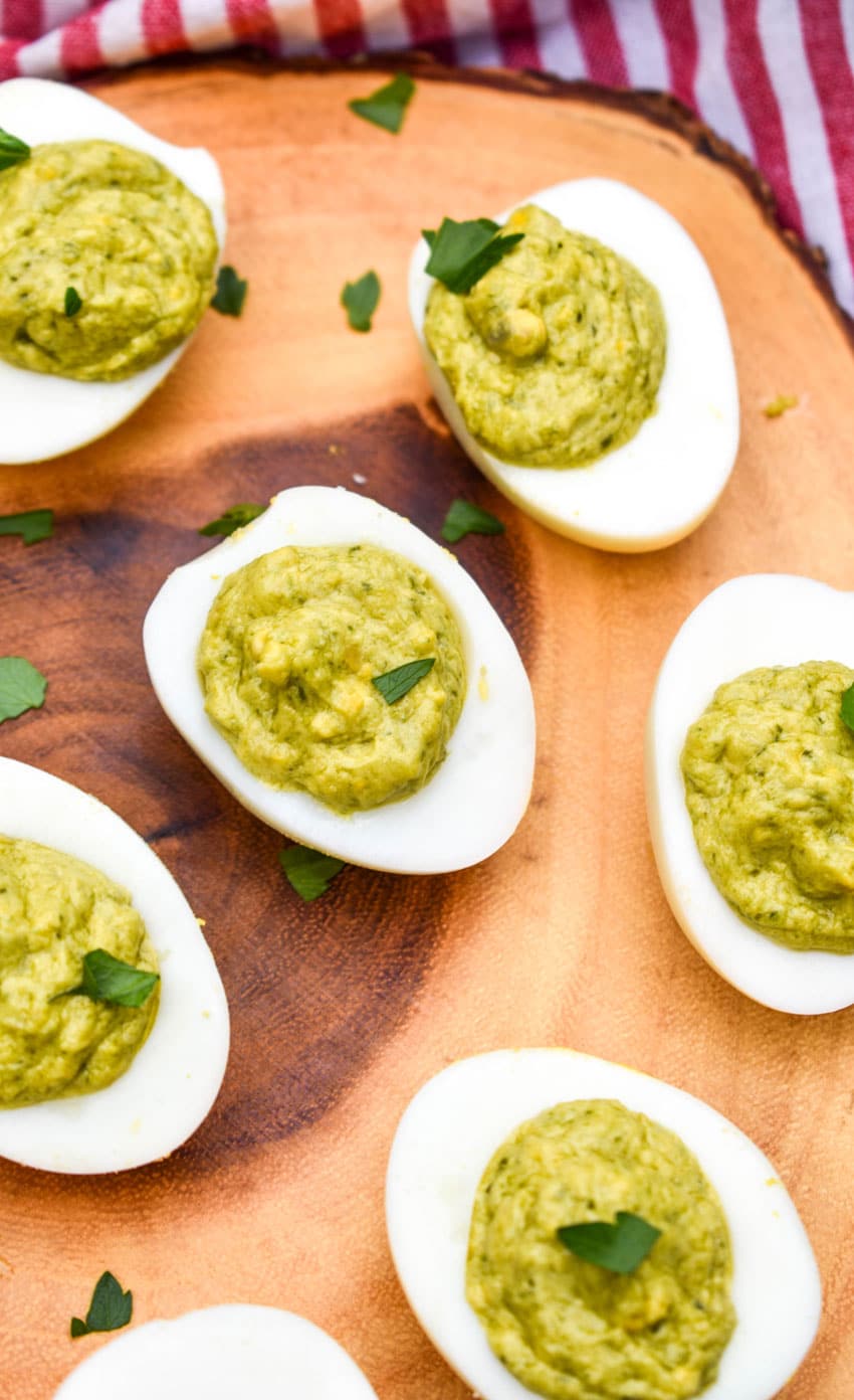 pesto deviled eggs topped with fresh parsley arranged on a wooden cutting board