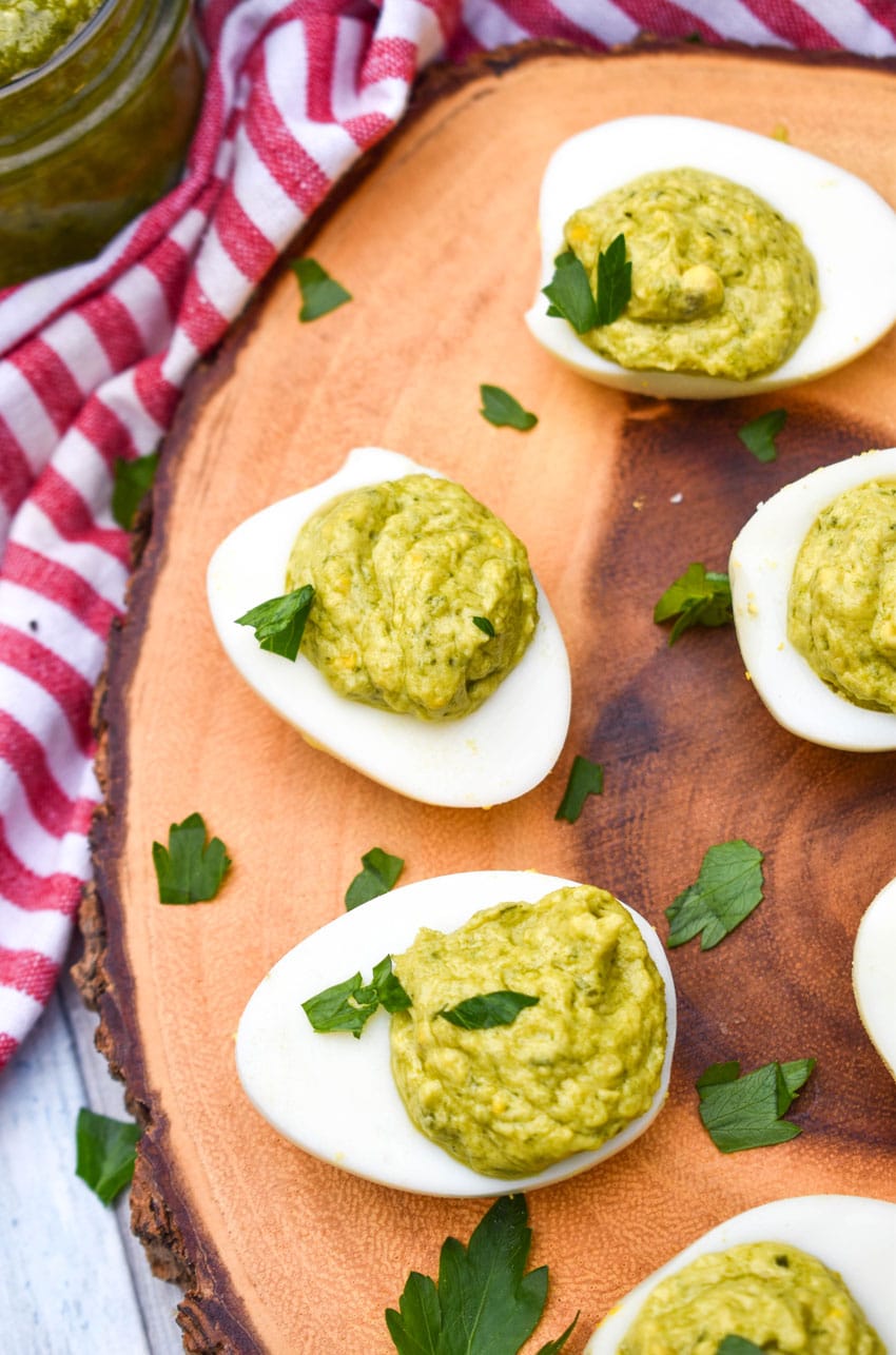 pesto deviled eggs topped with fresh parsley arranged on a wooden cutting board
