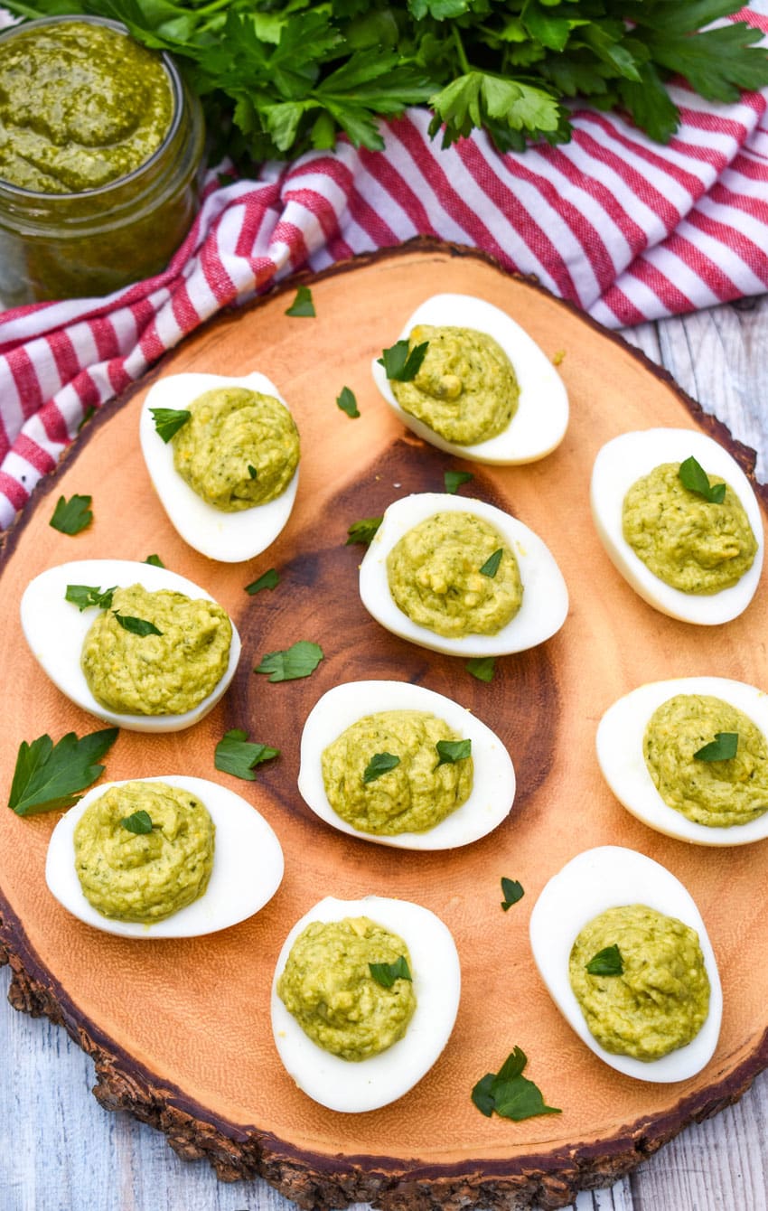 pesto deviled eggs topped with fresh parsley arranged on a wooden cutting board