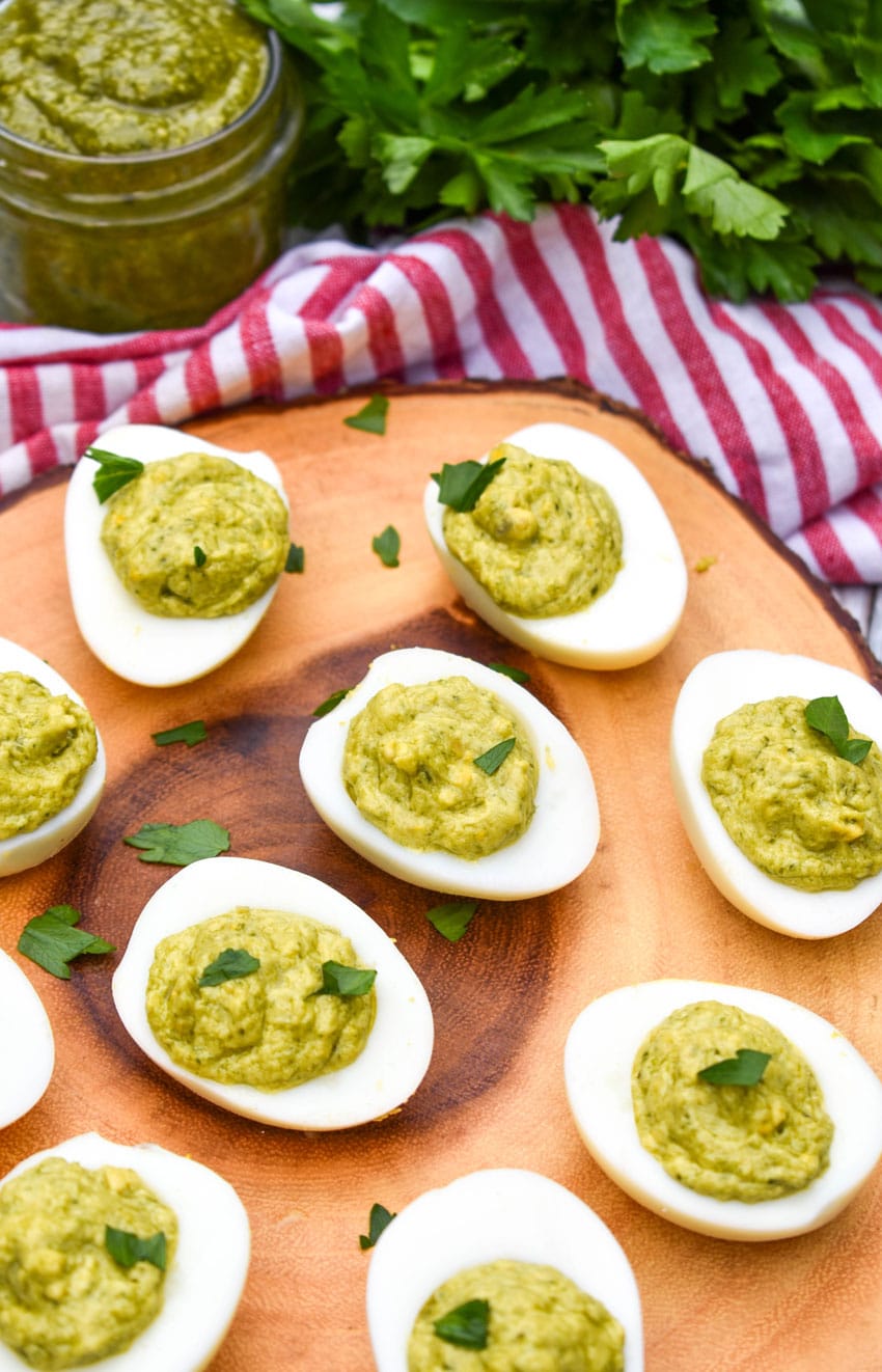 pesto deviled eggs topped with fresh parsley arranged on a wooden cutting board