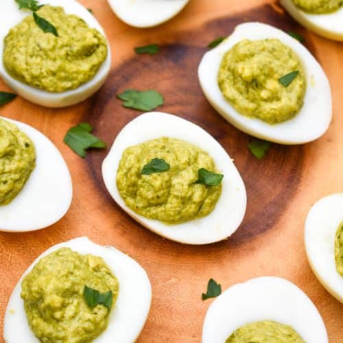 pesto deviled eggs topped with fresh parsley arranged on a wooden cutting board