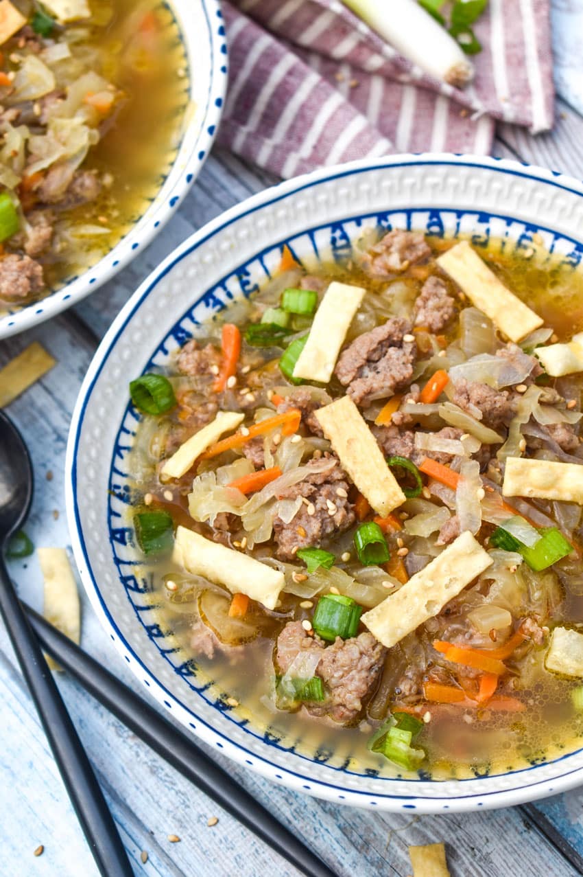 pork egg roll soup topped with crispy wonton strips in a white bowl with two black spoons on the side