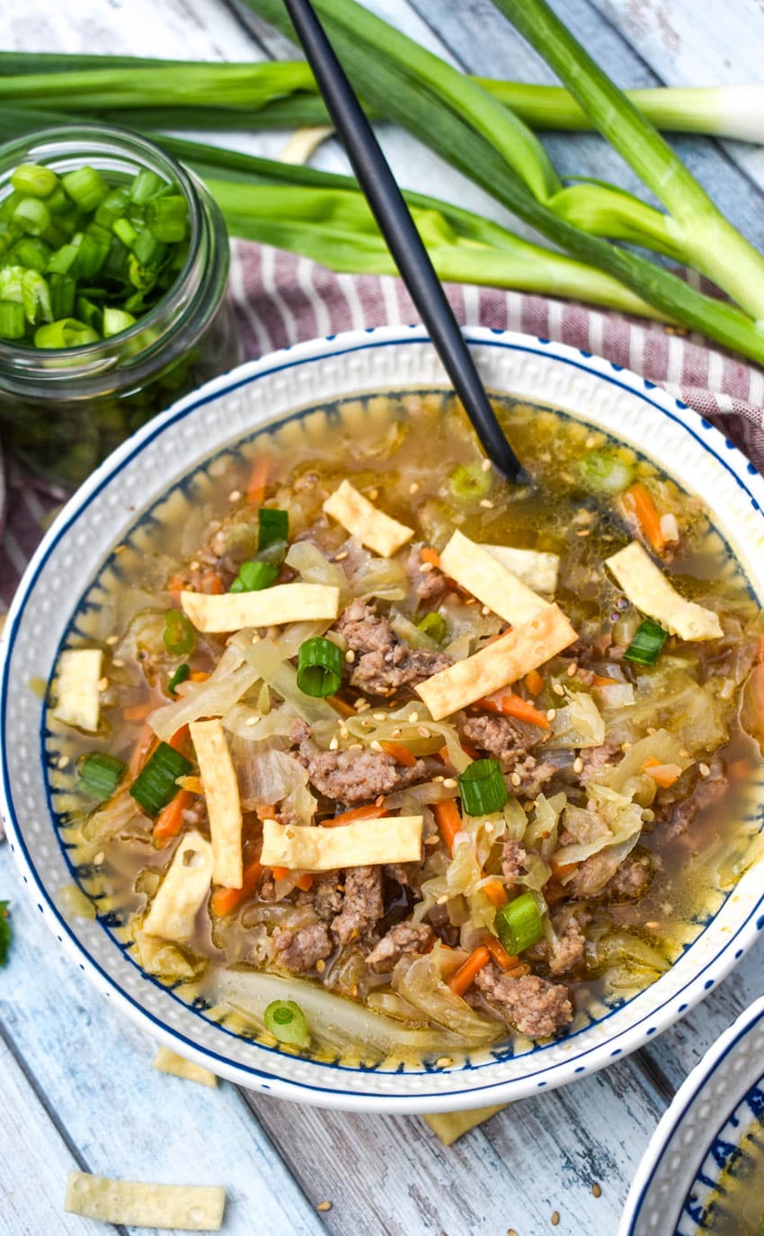 pork egg roll soup topped with crispy wonton strips in a white bowl with a black spoon resting on the side