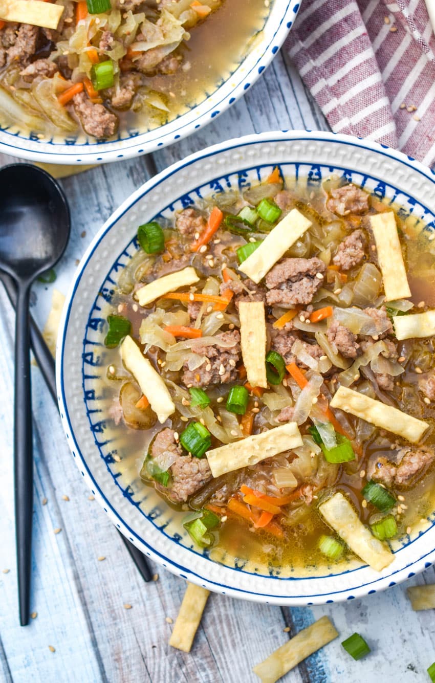 pork egg roll soup topped with crispy wonton strips in white bowls with black spoons on the side