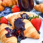 crockpot blueberry sauce spread over two croissants on a white plate with fresh fruit on the side