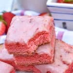 strawberry brownies stacked on a sheet of white parchment paper