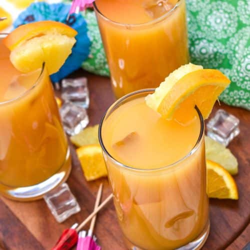copycat pog juice in small glasses with fresh fruit on the rims for garnish sitting on a wooden stand