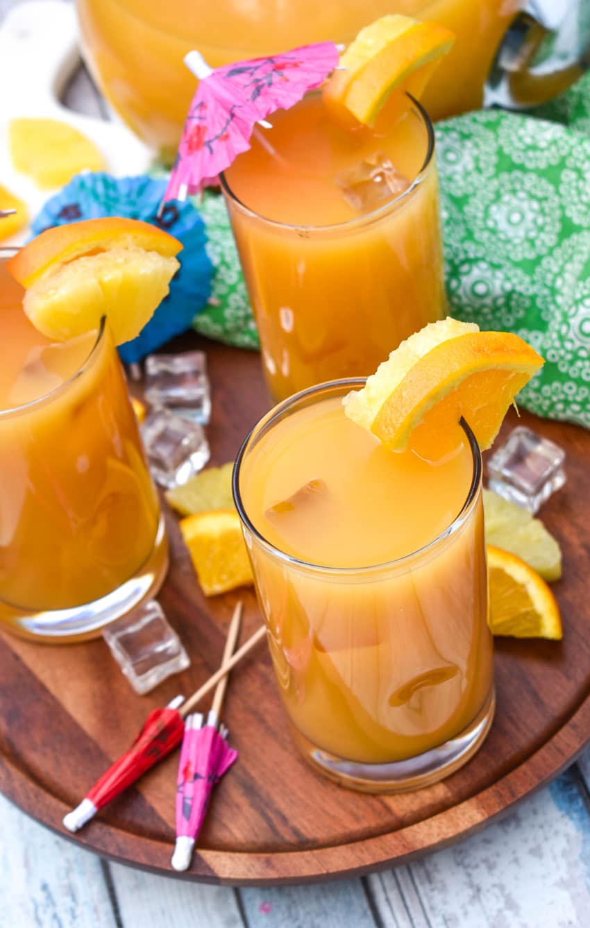copycat pog juice in small glasses with fresh fruit on the rims for garnish sitting on a wooden stand
