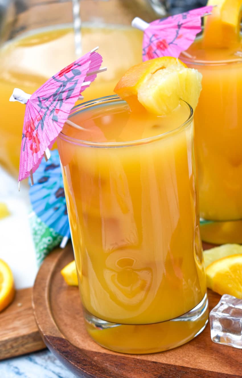 disney jungle juice in small glasses with fresh fruit on the rims for garnish sitting on a wooden stand 