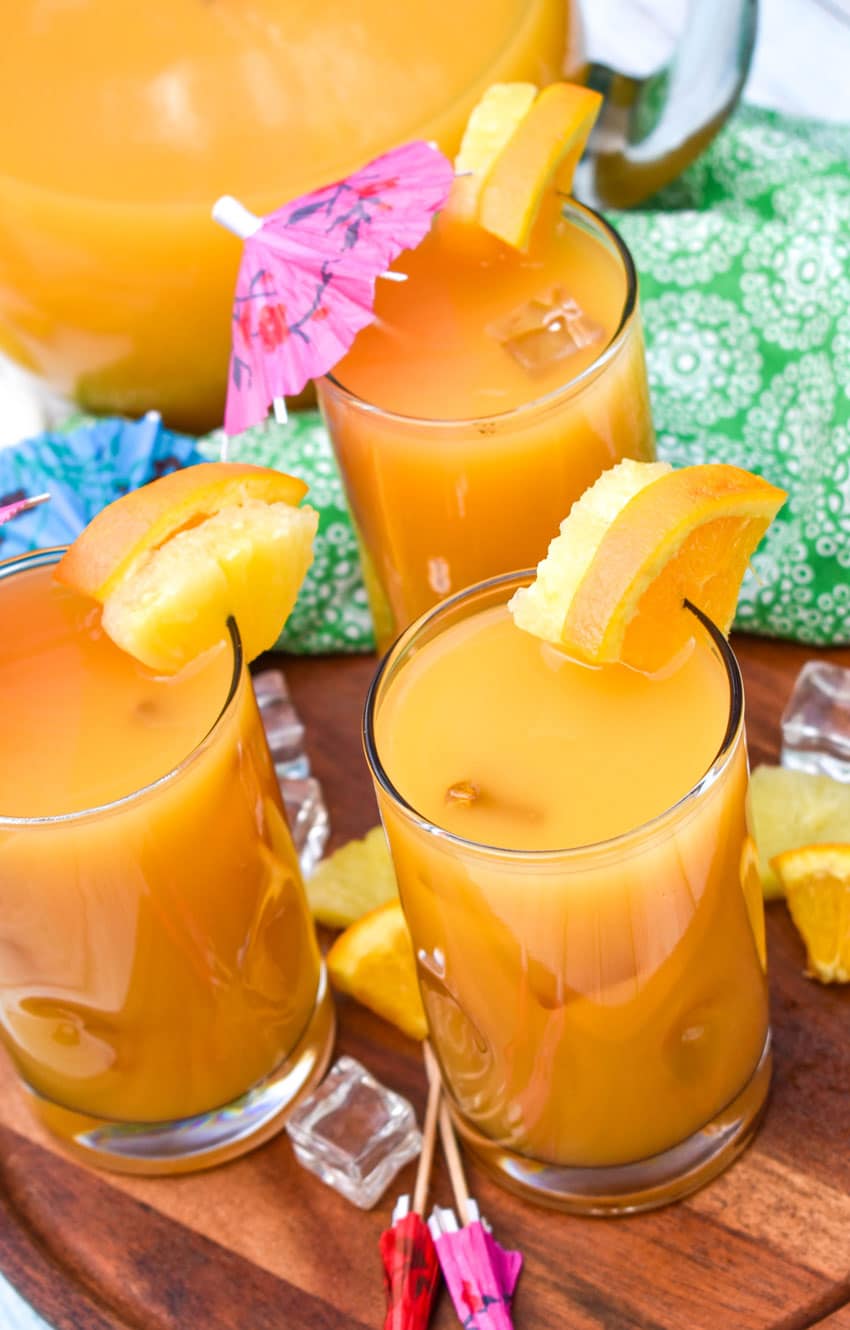 copycat pog juice in small glasses with fresh fruit on the rims for garnish sitting on a wooden stand 