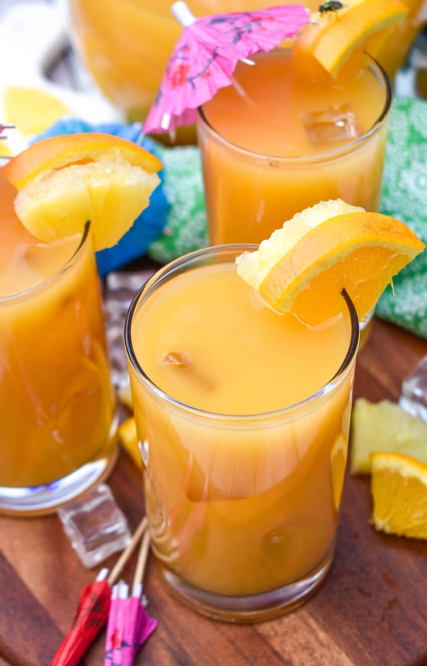 disney jungle juice in small glasses with fresh fruit on the rims for garnish sitting on a wooden stand 