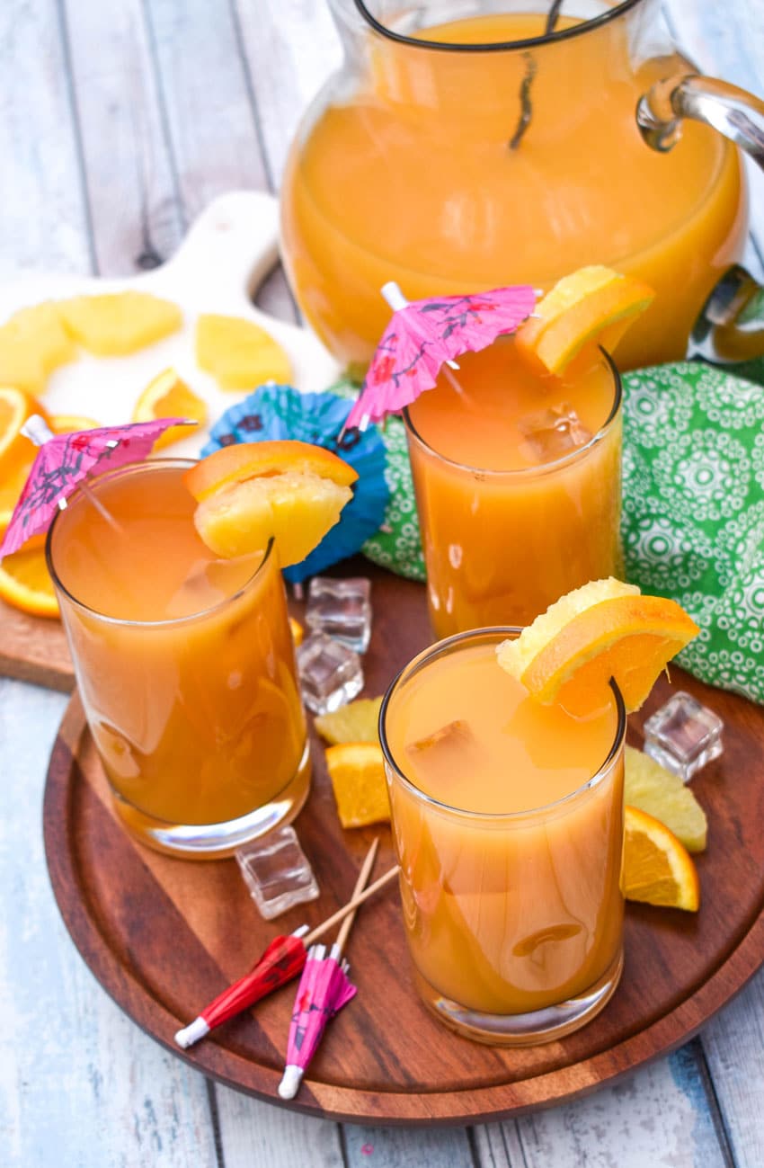 copycat pog juice in small glasses with fresh fruit on the rims for garnish sitting on a wooden stand 