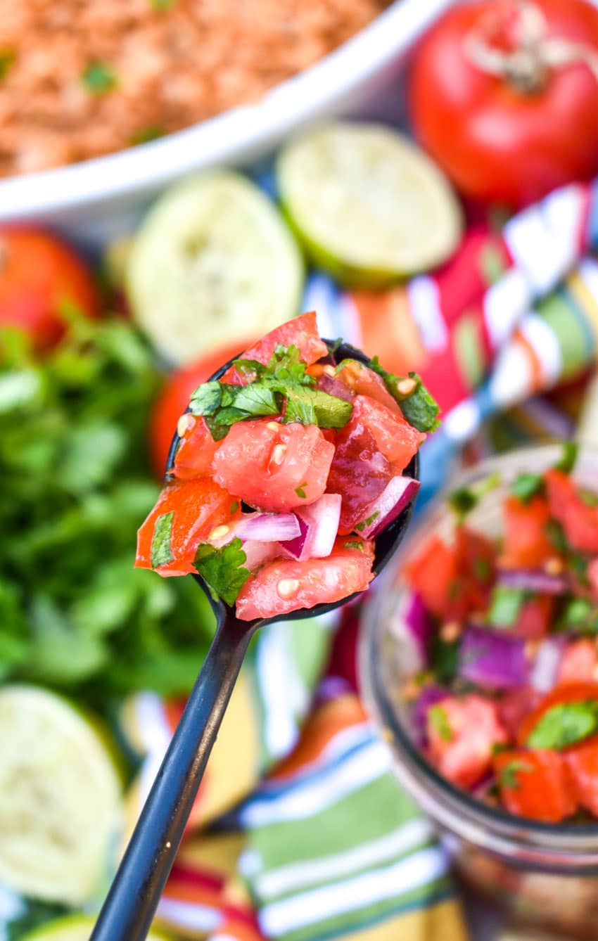 a black spoon holding up a scoop of homemade pico de gallo