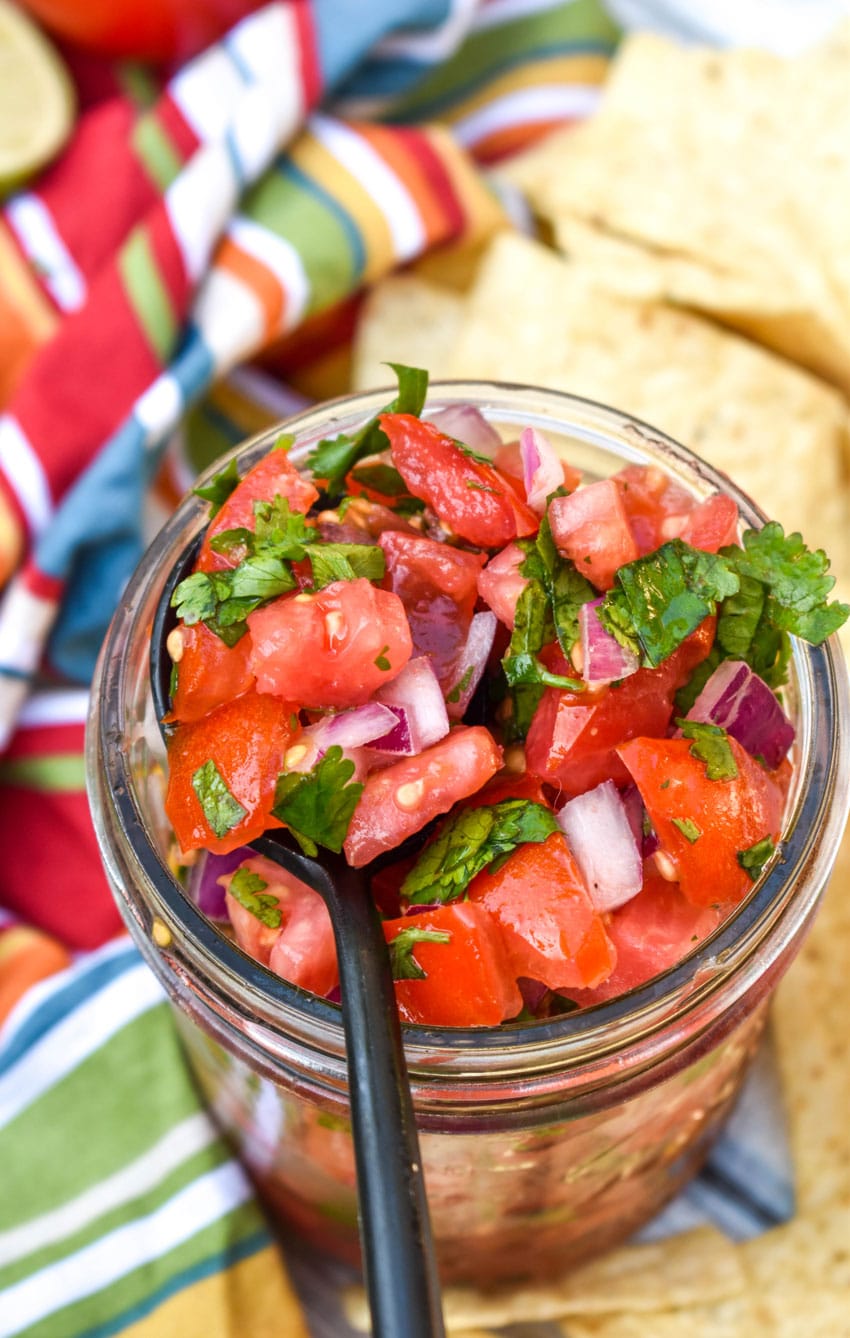 a black spoon scooping homemade pico de gallo from a small glass jar