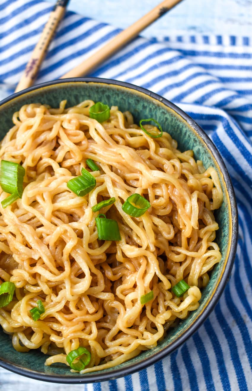 peanut butter ramen topped with sliced green onions in a bowl with wooden chop sticks on the side