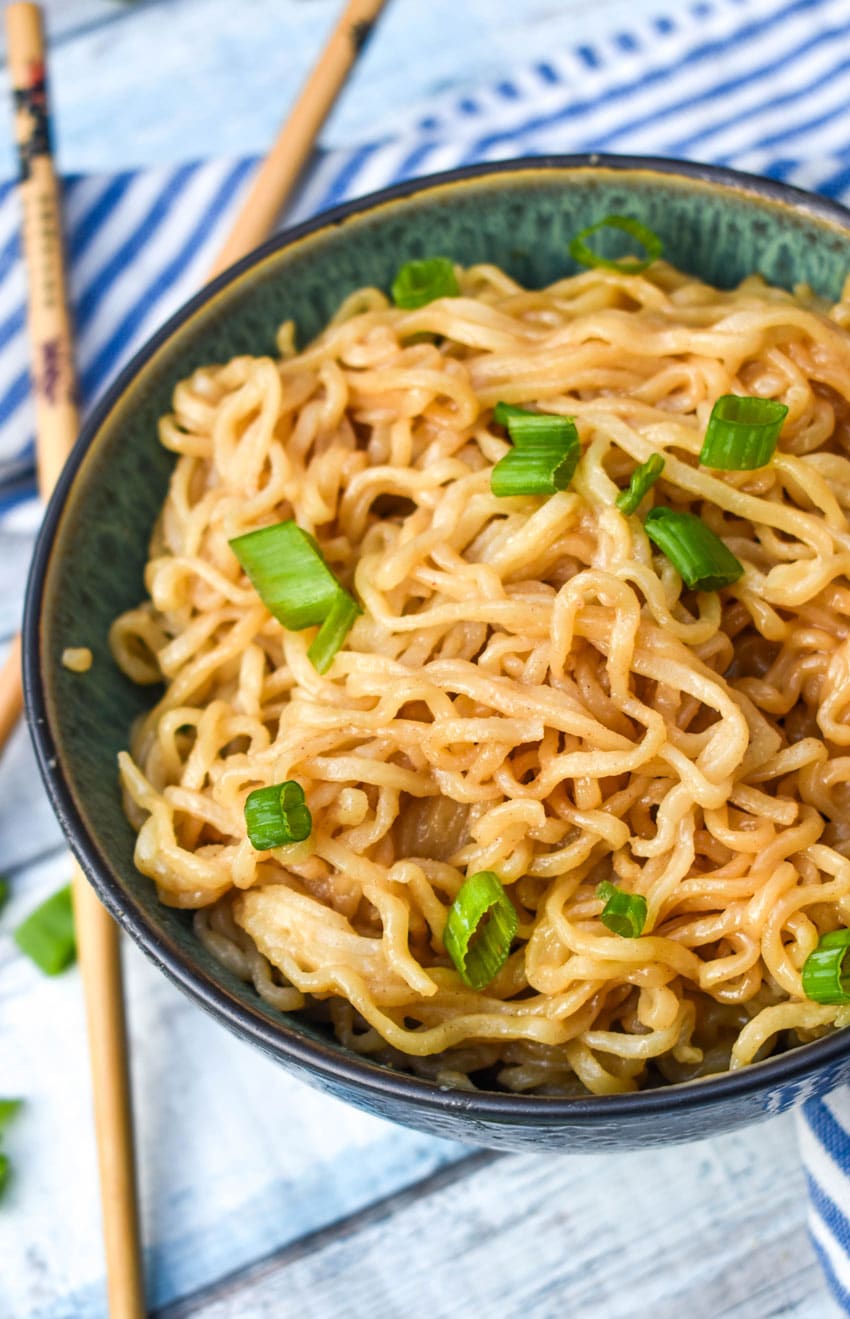 peanut butter ramen topped with sliced green onions in a bowl with wooden chop sticks on the side
