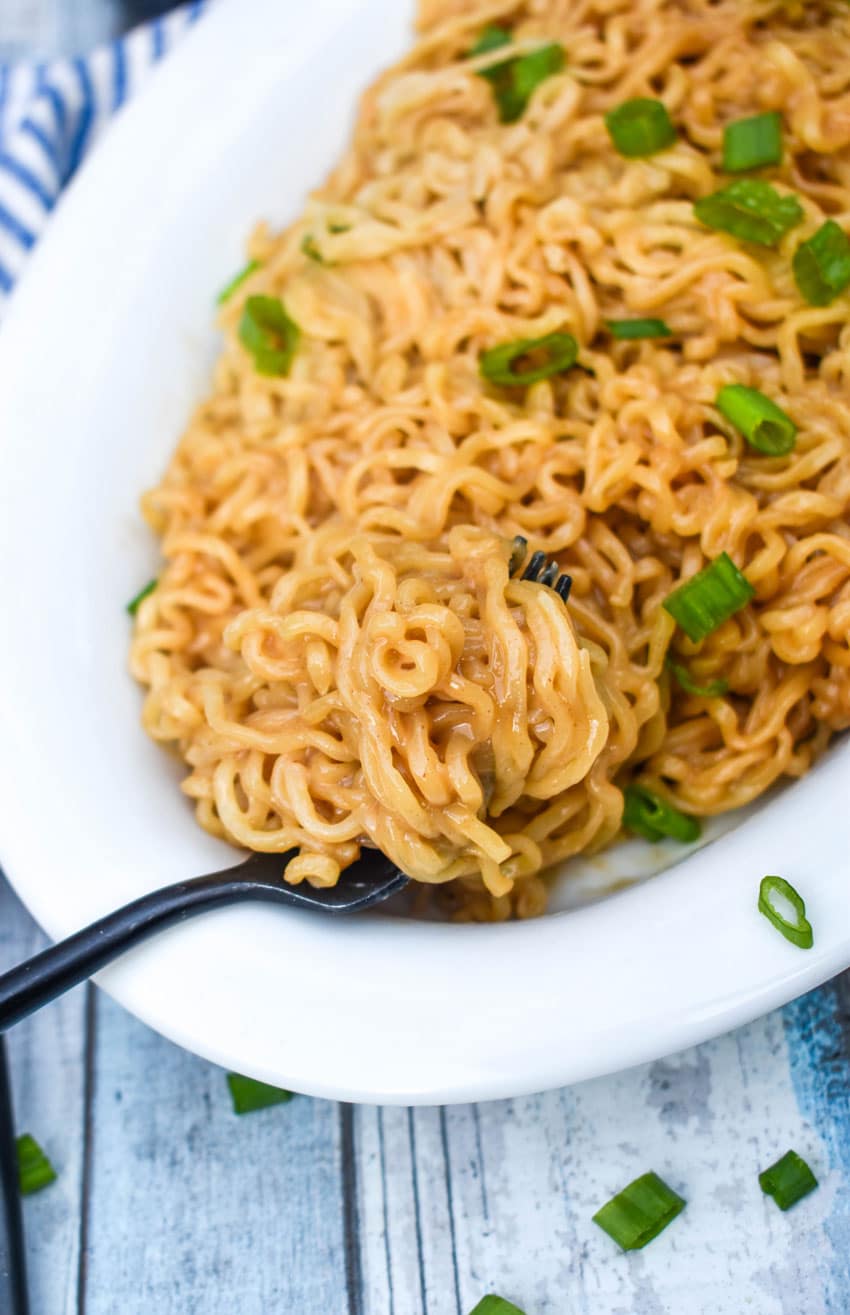 a black fork scooping peanut butter ramen noodles out of a white serving dish