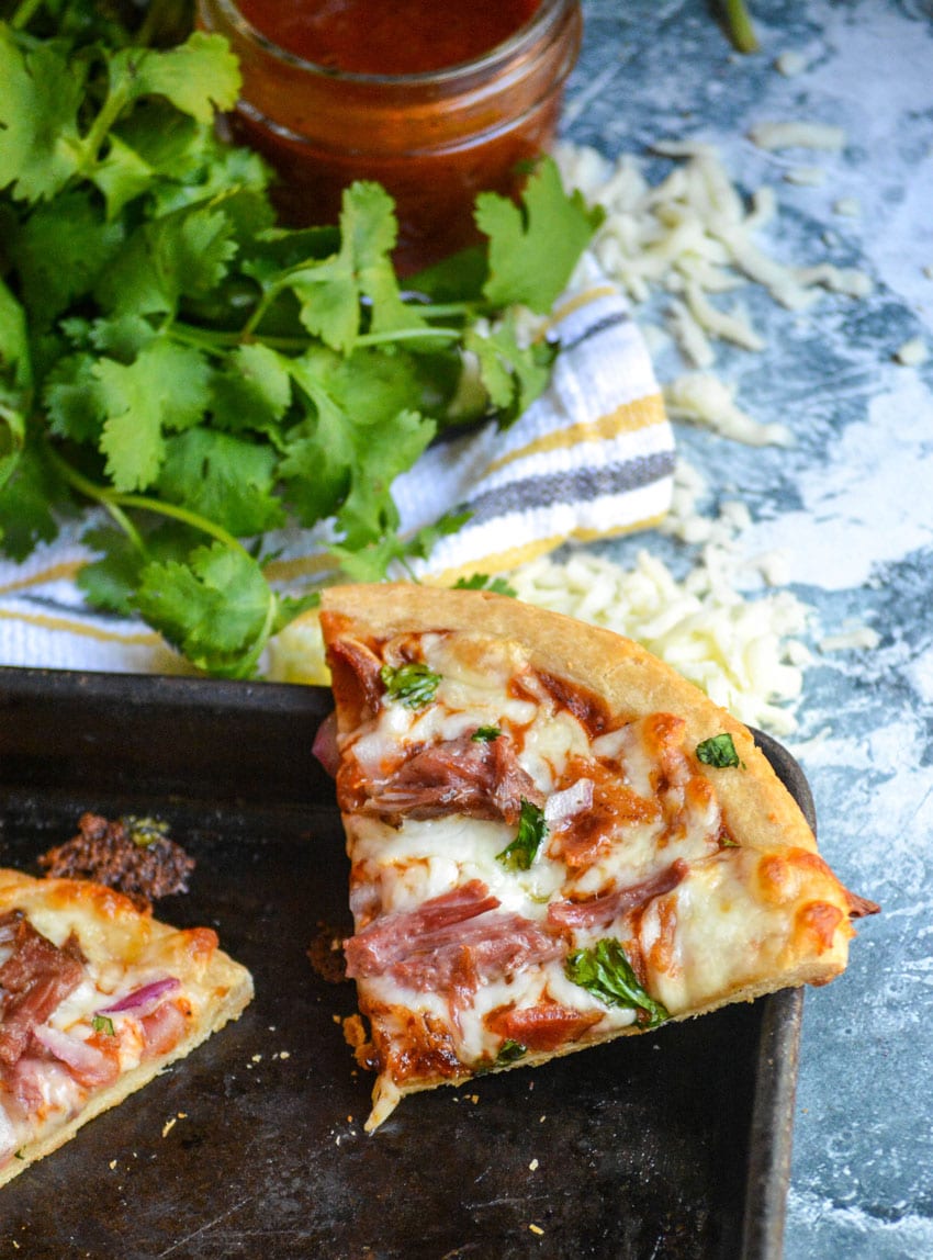 a slice of pulled pork pizza resting on the edge of a metal baking sheet