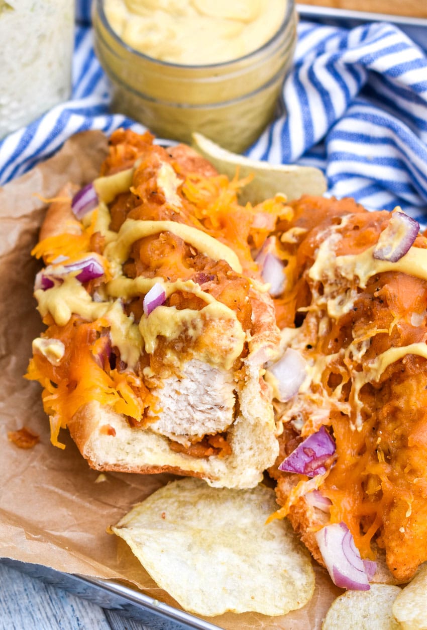 a bitten southern bird dog sandwich on a parchment paper lined metal serving tray with potato chips on the side