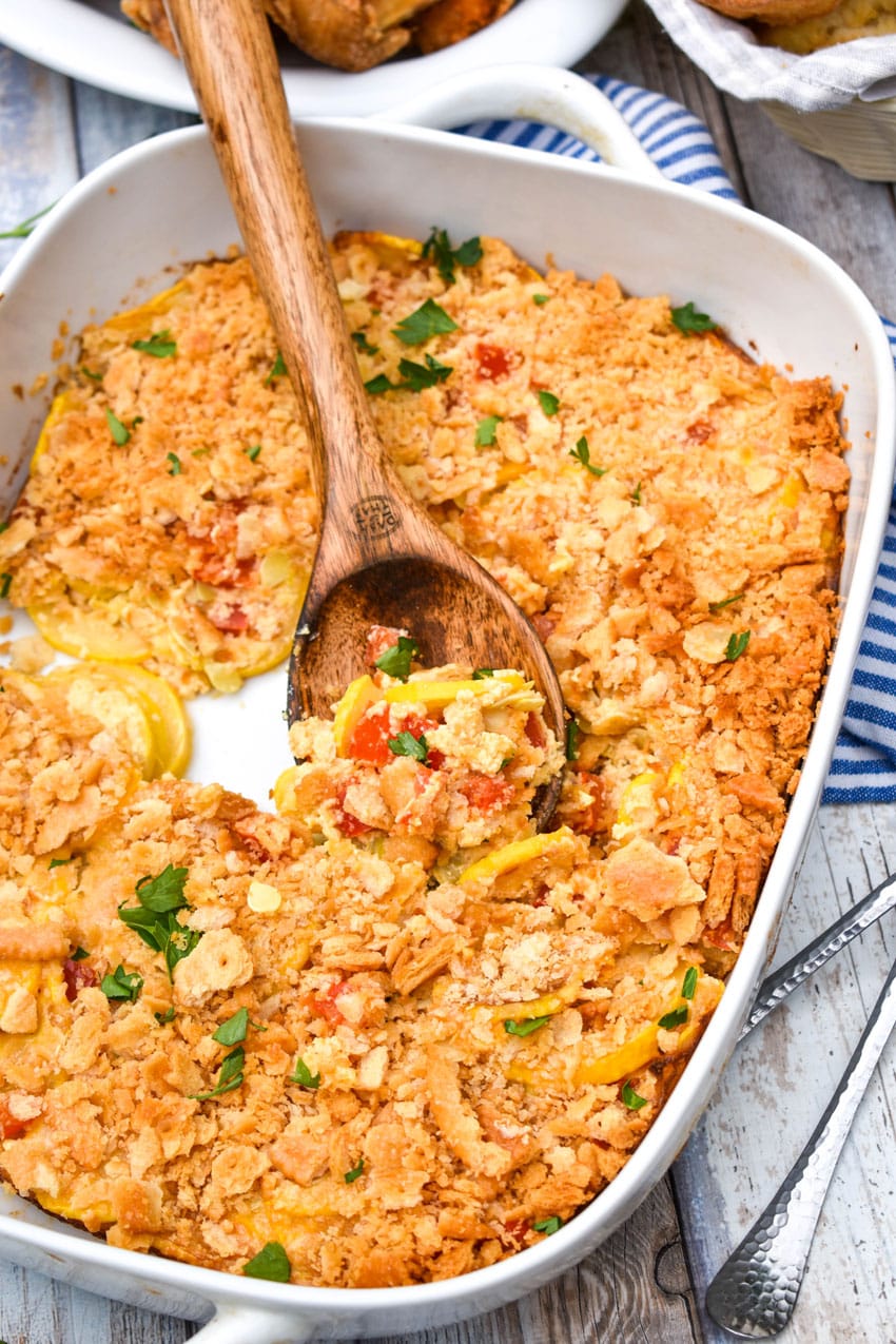 a wooden spoon scooping southern squash casserole out of a white baking dish