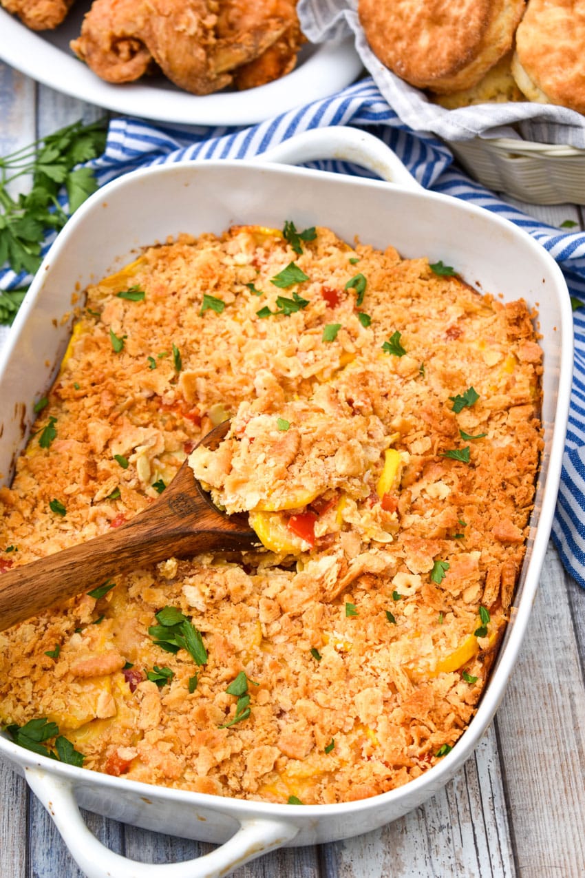a wooden spoon scooping southern squash casserole out of a white baking dish