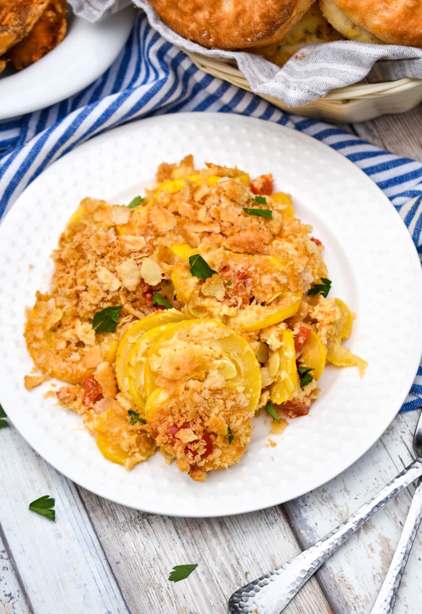 southern squash casserole on a small white plate with a basket of biscuits and platter of fried chicken on the side