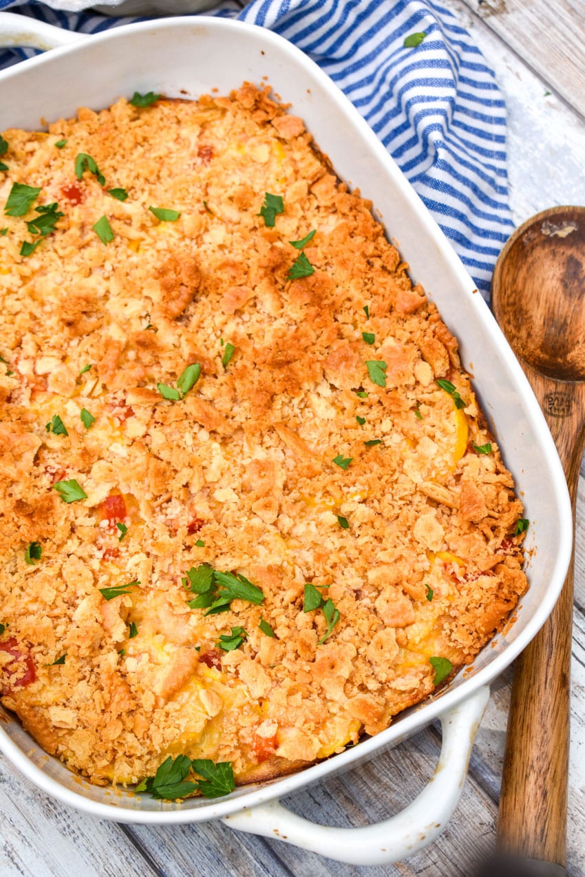southern squash casserole in a white baking dish with pieces of fresh parsley leaves on top