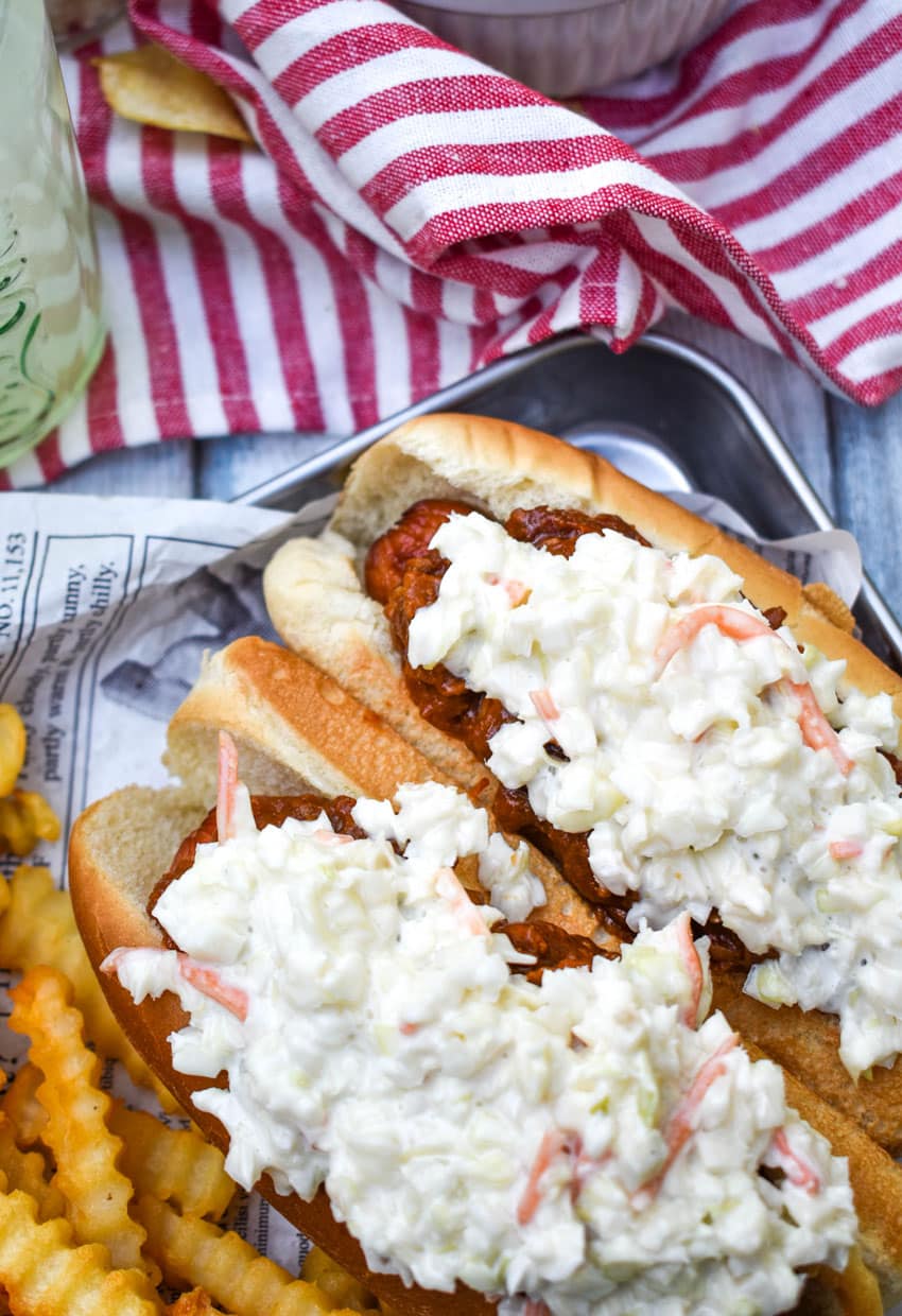 two carolina slaw dogs on a news paper lined metal serving tray with crinkle cut french fries on the side