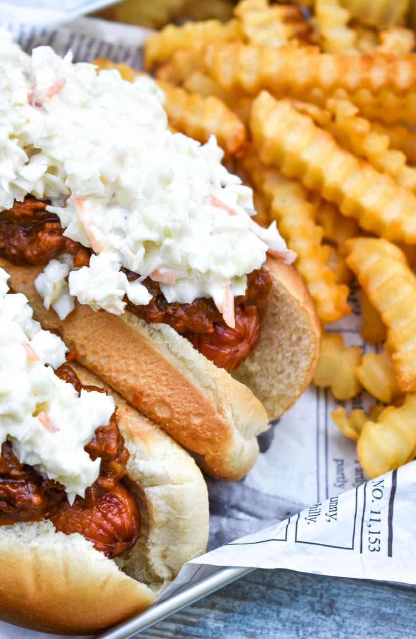 two carolina slaw dogs on a news paper lined metal serving tray with crinkle cut french fries on the side